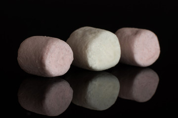 Group of three whole pink and white sweet fluffy marshmallow isolated on black glass