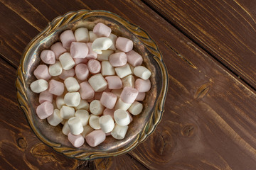 Lot of whole sweet fluffy marshmallow in old iron bowl flatlay on brown wood