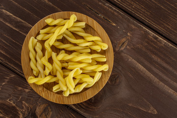 Lot of whole raw pasta gemelli on bamboo plate flatlay on brown wood