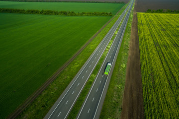 green truck driving on asphalt road along the green fields. seen from the air. Aerial view landscape. drone photography.  cargo delivery