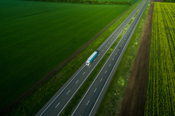 white truck driving on asphalt road along the green fields. seen from the air. Aerial view landscape. drone photography.  cargo delivery