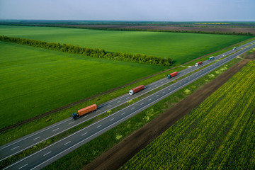 truck convoy on the higthway sunset. cargo delivery driving on asphalt road along the green fields....