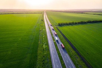 trucks on the higthway sunset. cargo delivery driving on asphalt road along the green fields. seen...
