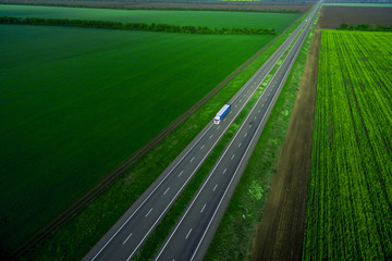 white truck on the higthway sunset. cargo delivery driving on asphalt road along the green fields. seen from the air. Aerial view landscape. drone 