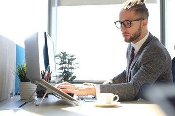 Good looking young man in full suit using laptop while sitting in the office.