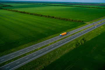 orange truck driving on asphalt road along the green fields. seen from the air. Aerial view...