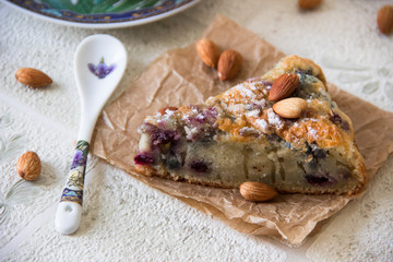 The slice of cake with berries decorated with powdered sugar and almonds. The slice of cake on a craft napkin, spoon and cup of tea on the table. Homemade bakery cake. Breakfast dessert. Food concept.