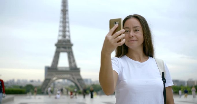 tourist woman is taking selfie with Eiffel tower in Paris in daytime, using smartphone