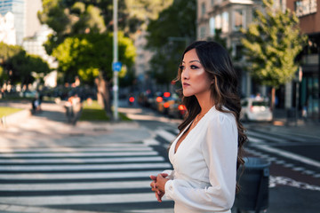 Summer sunny lifestyle portrait of young stylish asian girl on the street of big modern city. She wears white dress