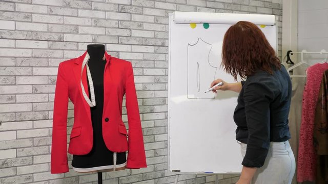 Handmade clothes cutting and sewing. Dressmaker draws a pattern of jacket on white board in sewing workshop. Clothes designer creates new model of jacket. Woman at work in tailoring business.
