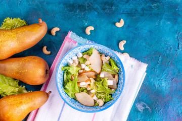 Fresh salad with lettuce leaves, pear, nuts and feta cheese in blue plate. healthy vegetarian food. top view
