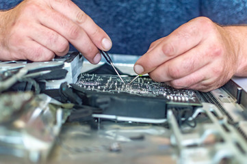 a man repairs a computer, solders a board, repairs electronics and modern technologies