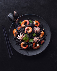 Modern Japanese dinner, Mediterranean cuisine. Black spaghetti ink black cuttlefish ink with seafood, shrimp, mussels, octopus on black background. The view from the top. Copy space - 283389214