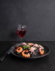 Black spaghetti. Black seafood pasta with octopus, shrimp and mussels and a glass of red wine on a black background. Copy space - 283389249