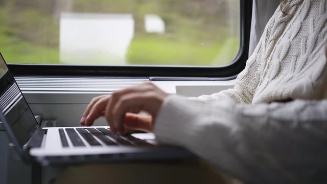 Young girl travelling on train in daytime. Woman sitting near window, working on computer. Detail view female hands opening notebook and starts typing on keyboard. Concept freelancer job in journey 