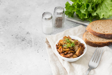 Fried chanterelles with onions in a white plate on a light gray table