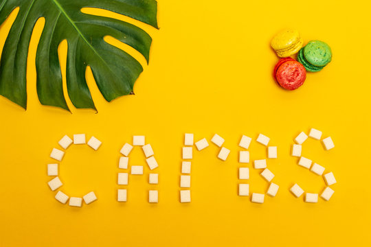 The "CARBS" word made of sugar cubes with macaroons and leaf of ceriman on bright yellow background