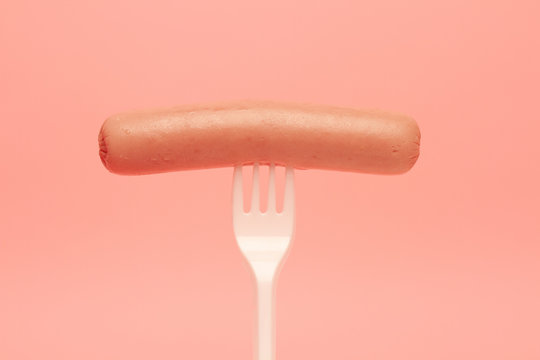 Sausage on the plastic fork. Pink background. Fast food