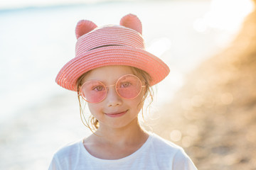 Smiling child girl in pink hat and sunglasses on the ocean coastline