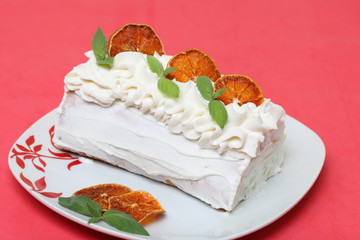 Sponge cream cake coated with cream and garnished with dried orange slices and fresh mint leaves. Against the background of coral color.