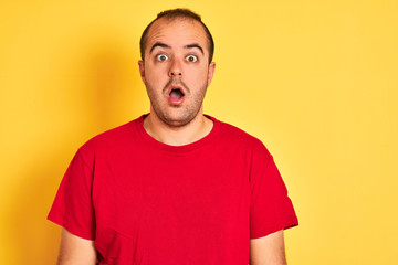 Obraz premium Young man wearing red casual t-shirt standing over isolated yellow background scared in shock with a surprise face, afraid and excited with fear expression