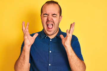 Young man wearing denim casual shirt standing over isolated yellow background celebrating mad and...