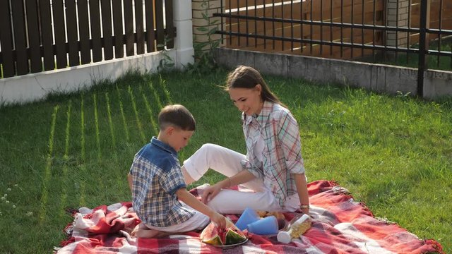 pretty young mother with loose dark hair sits and feeds son with raspberries on green grass close view slow motion