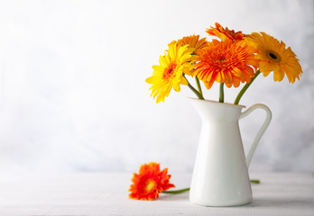 Beautiful bouquet of red and yellow flowers in white vase on wooden table, front view. Autumn still life with flowers.