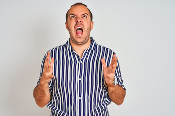 Fototapeta premium Young man wearing blue striped shirt standing over isolated white background crazy and mad shouting and yelling with aggressive expression and arms raised. Frustration concept.
