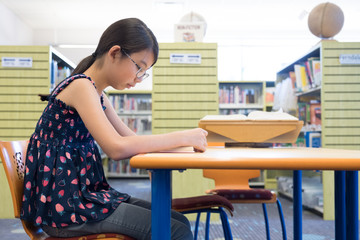 Portrait of young Asian girl reading book in library