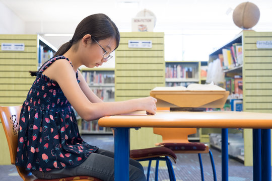 Portrait Of Young Asian Girl Reading Book In Library