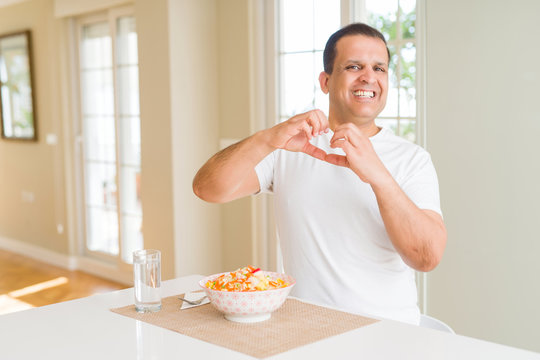 Middle age man eating rice at home smiling in love showing heart symbol and shape with hands. Romantic concept.