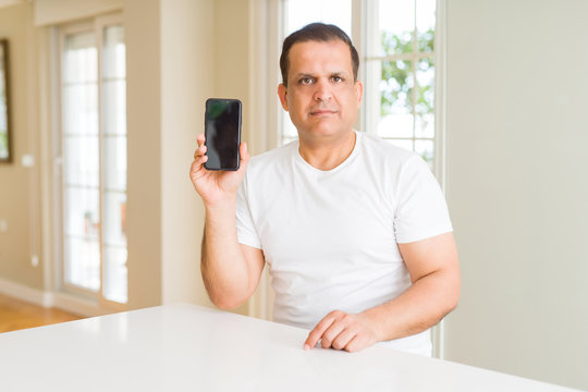 Middle age man showing smartphone screen with a confident expression on smart face thinking serious