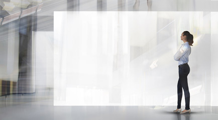 Fototapeta premium Young woman in front of big white banner in the open exhibition or industrial space. Space for your image or text. Business and strategy concept