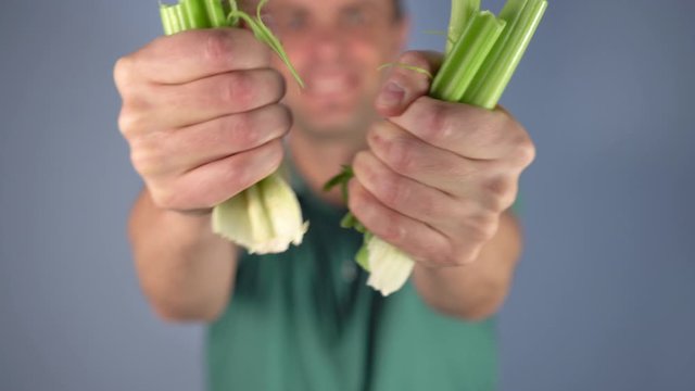 A man in a green T-shirt breaks a bunch of celery on a blue background. Selective focus. The concept of winning a healthy diet and cooking diet at home