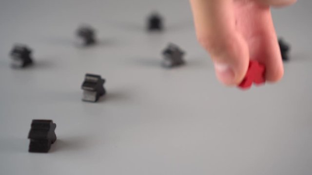 The hand removes the red figure from the environment of black figures on a gray surface. The concept of the dismissal of the leader from the team