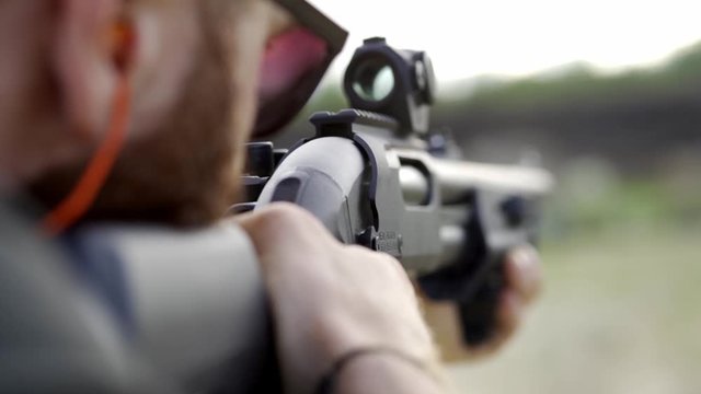 Courageous man with a beard in glasses, shoots from a shotgun in the open air. Close up, slow mo.