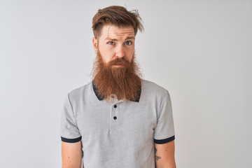 Young redhead irish man wearing grey polo standing over isolated white background skeptic and nervous, frowning upset because of problem. Negative person.