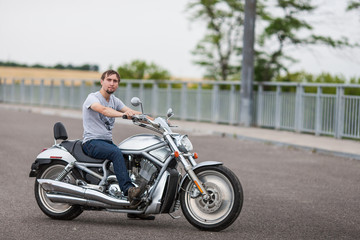 Fototapeta na wymiar Handsome rider man sitting on classic style cruiser motorbike on an open road. Brutal young man sitting at powerful shiny style cruiser motorbike on highway