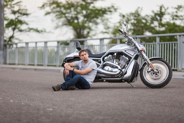 Fototapeta na wymiar Handsome rider man sitting near classic style cruiser motorbike on an open road. Brutal young man sitting at powerful shiny style cruiser motorbike on highway