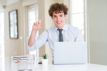 Young business man working with computer laptop at the office smiling and confident gesturing with hand doing size sign with fingers while looking and the camera. Measure concept.