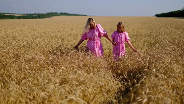 Front view of mother and daughter in the same dresses walking in a wheat field, nature