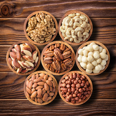 various nuts in wooden bowls, top view. food background: pecan, hazelnut, walnuts, almonds, macadamia, cashew, brazil