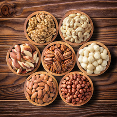 various nuts in wooden bowls, top view. food background: pecan, hazelnut, walnuts, almonds,...