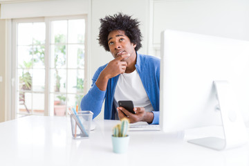 African American man working using smartphone and computer serious face thinking about question,...