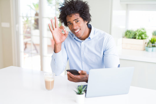 African American business man using smartphone and laptop doing ok sign with fingers, excellent symbol
