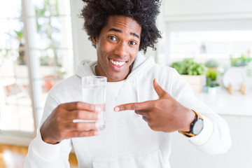 African American man drinking a glass of water at home very happy pointing with hand and finger