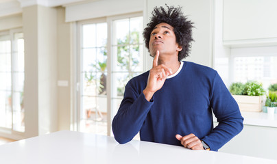 Fototapeta na wymiar Young african american man wearing casual sweater sitting at home Thinking concentrated about doubt with finger on chin and looking up wondering