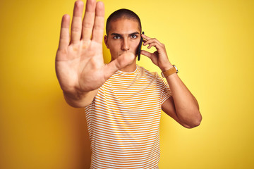 Young handsome man talking using smartphone over yellow isolated background with open hand doing...