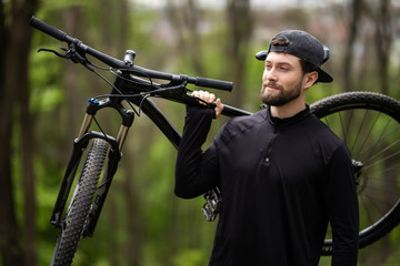 Male mountain biker carrying bicycle in the forest on a sunny day